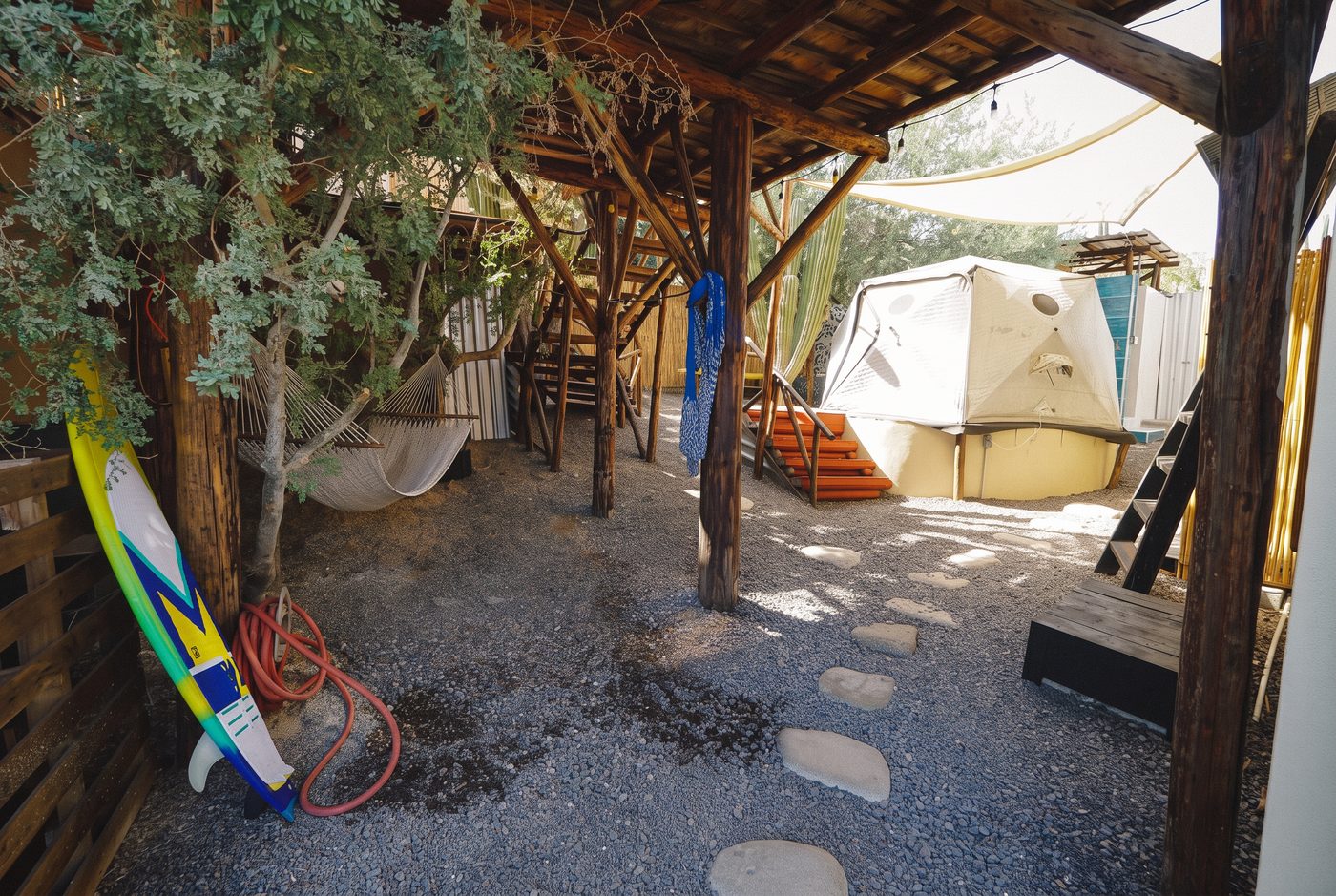 The shaded gravel patio with hammocks, a surfboard and a tent on its platform