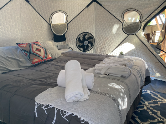 Glamping Andromeda — inside the dome: double bed with grey bedding, a woven cushion and folded white robes