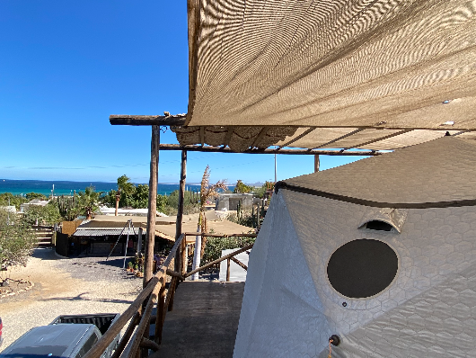 Glamping Aries — terrace with log railing and shade sail, sea and cactus views