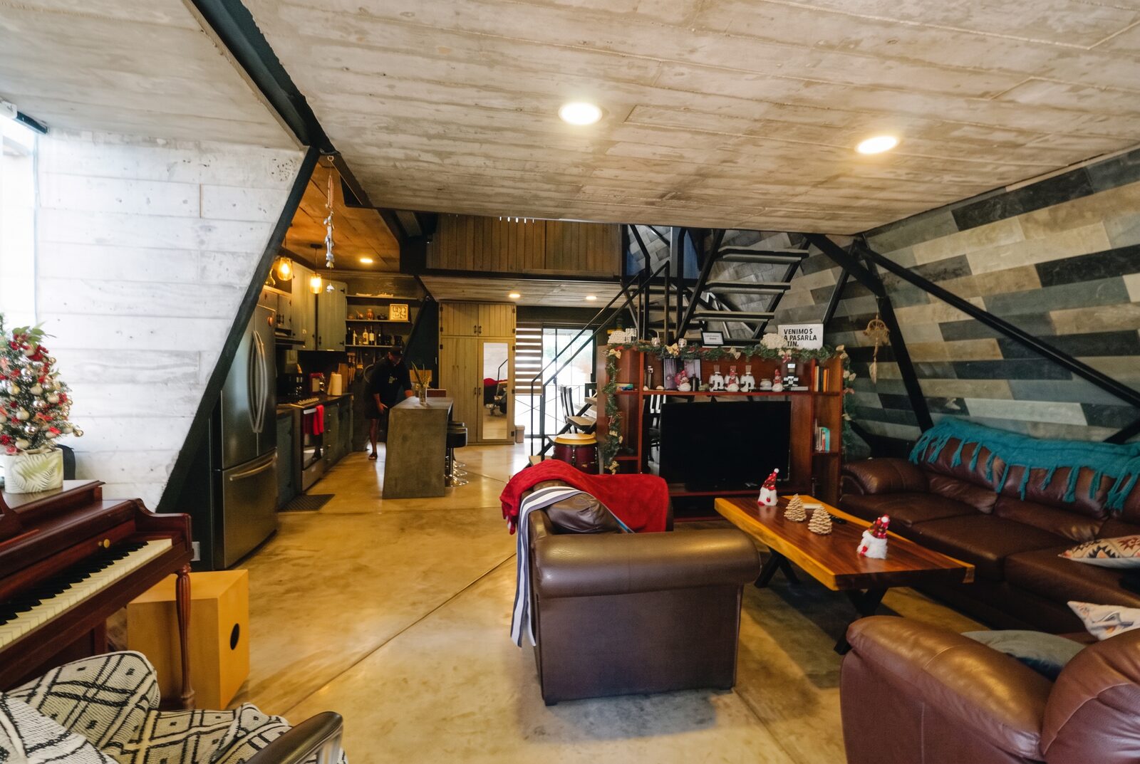 The common room and kitchen of the house, with sofas, a piano and the staircase