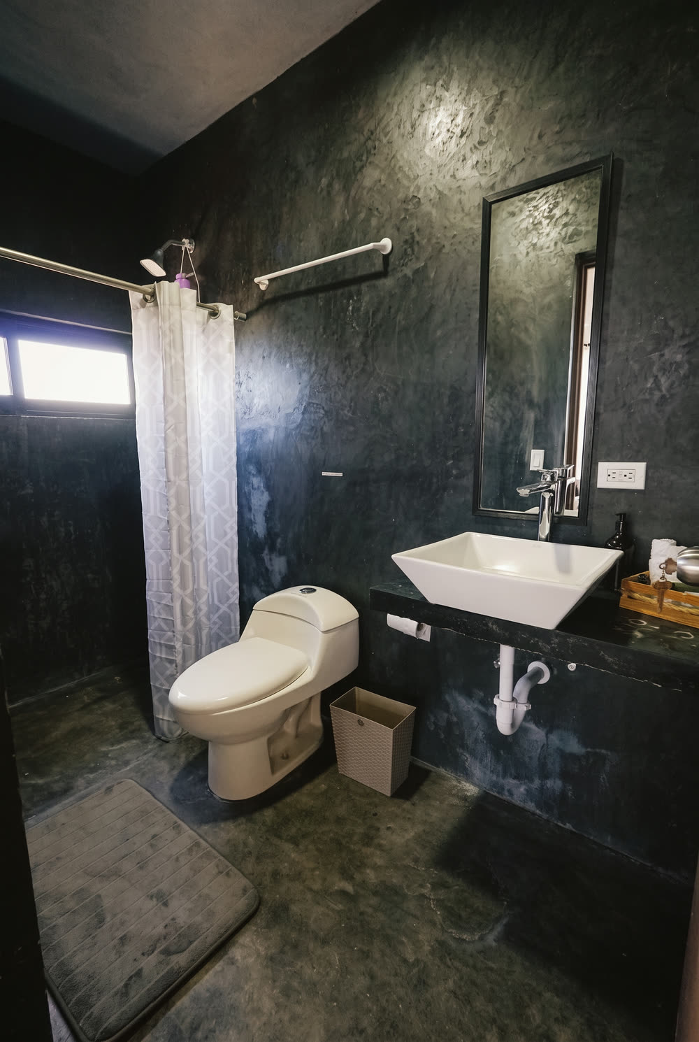 Master Suite bathroom — dark polished concrete walls, white vessel sink on a black counter and a mirror