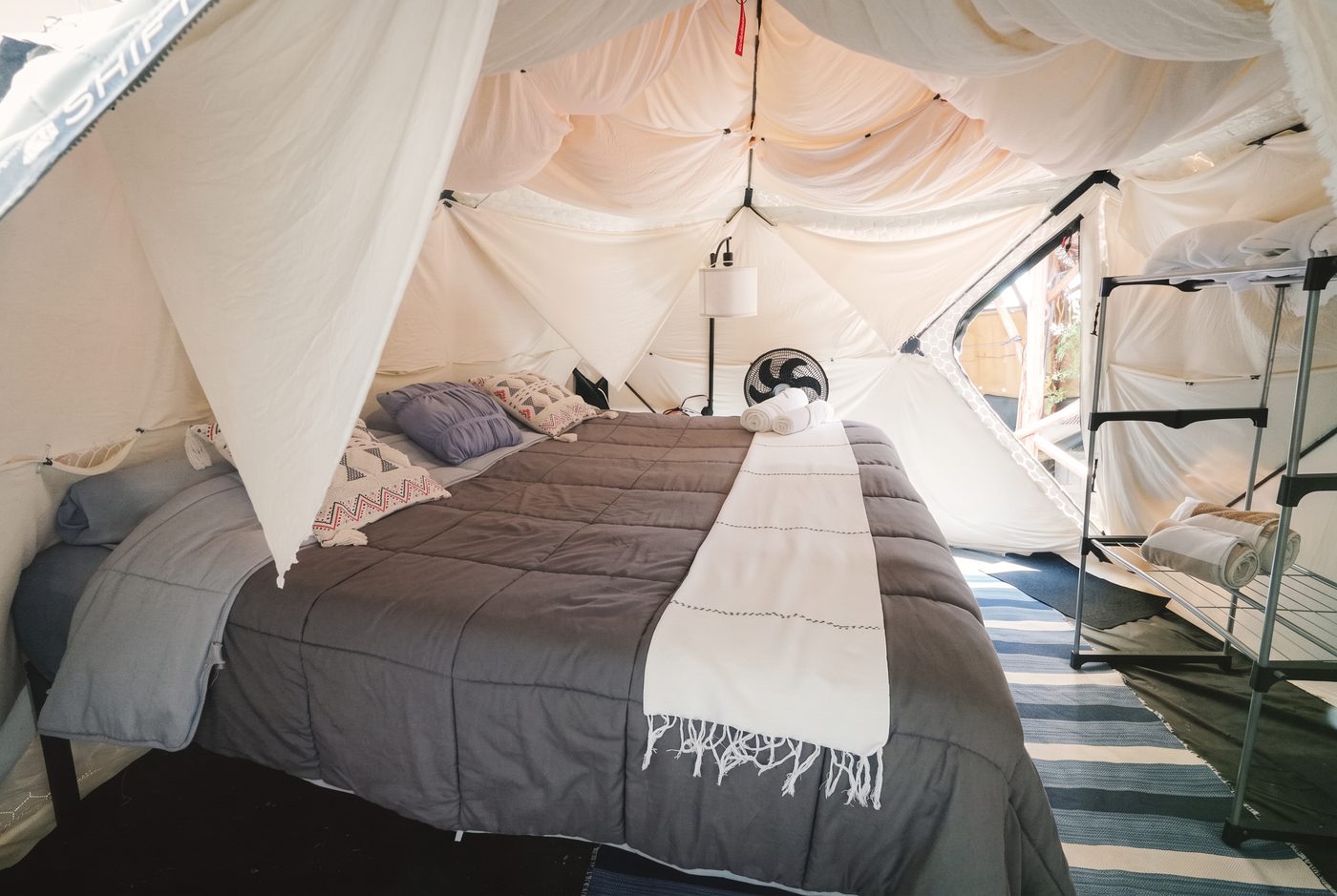 Inside a tent — a king bed under soft canopy fabric, with a striped rug